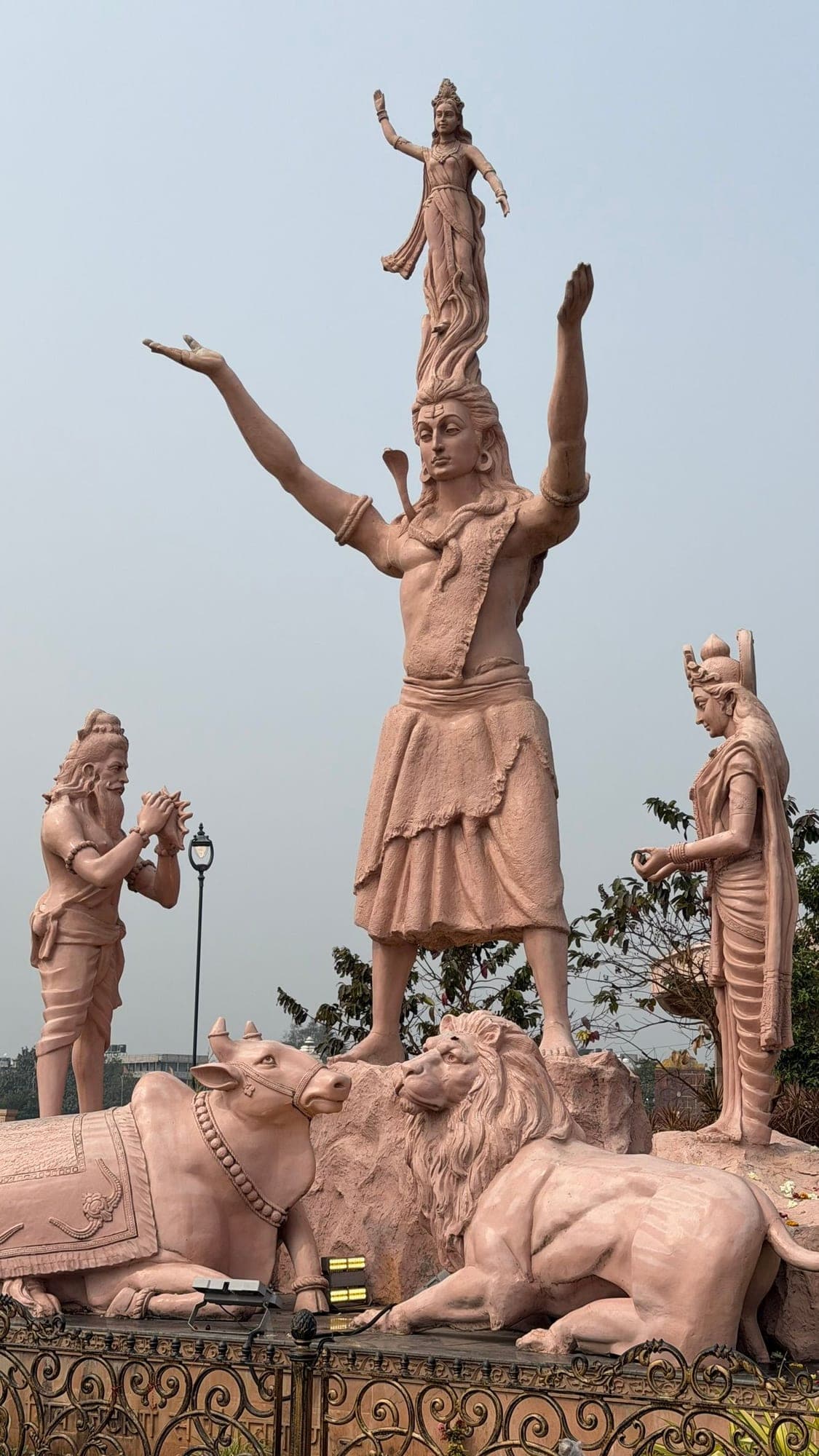 A group of pinkish-brown statues: a tall figure of Shiva with raised arms and a small dancing figure on his head, a kneeling figure at the left, a standing figure at the right, and a bull and a lion at the base
