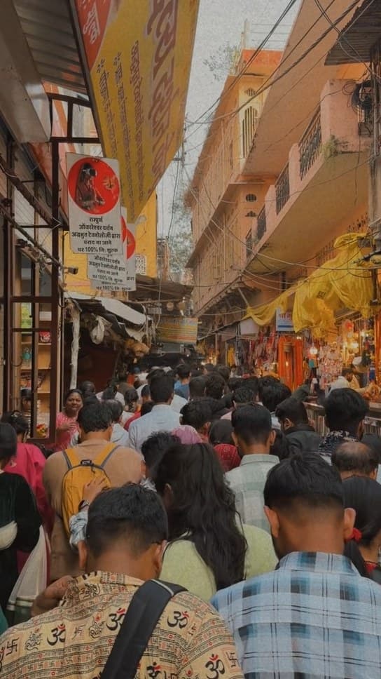 A crowded market lane seen from behind the crowd, with shops, yellow awnings and Hindi signboards on both sides